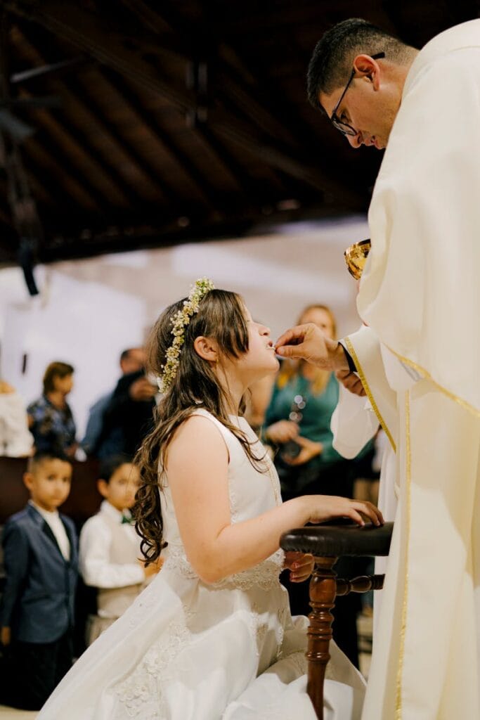 A young girl receiving her first communion from a priest during a church ceremony.