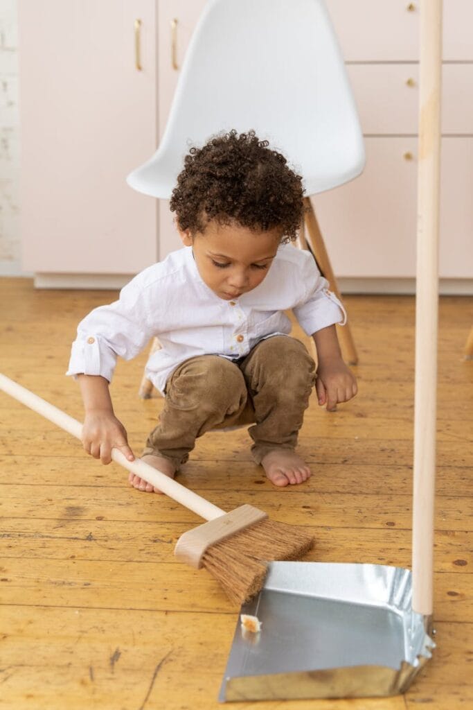 Adorable child sweeping a hardwood floor indoors, showcasing innocence and responsibility.