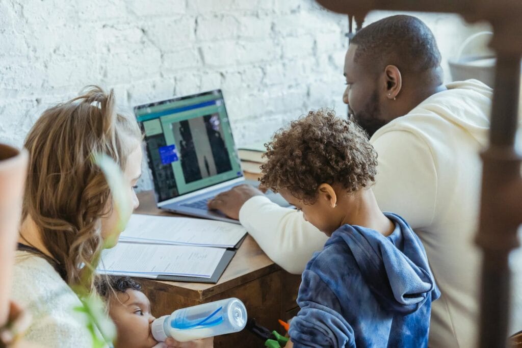 High angle of African American dad watching laptop working near son playing toys and mother feeding little infant