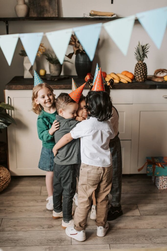 Group of kids hugging and smiling at a birthday party indoors with decorations.