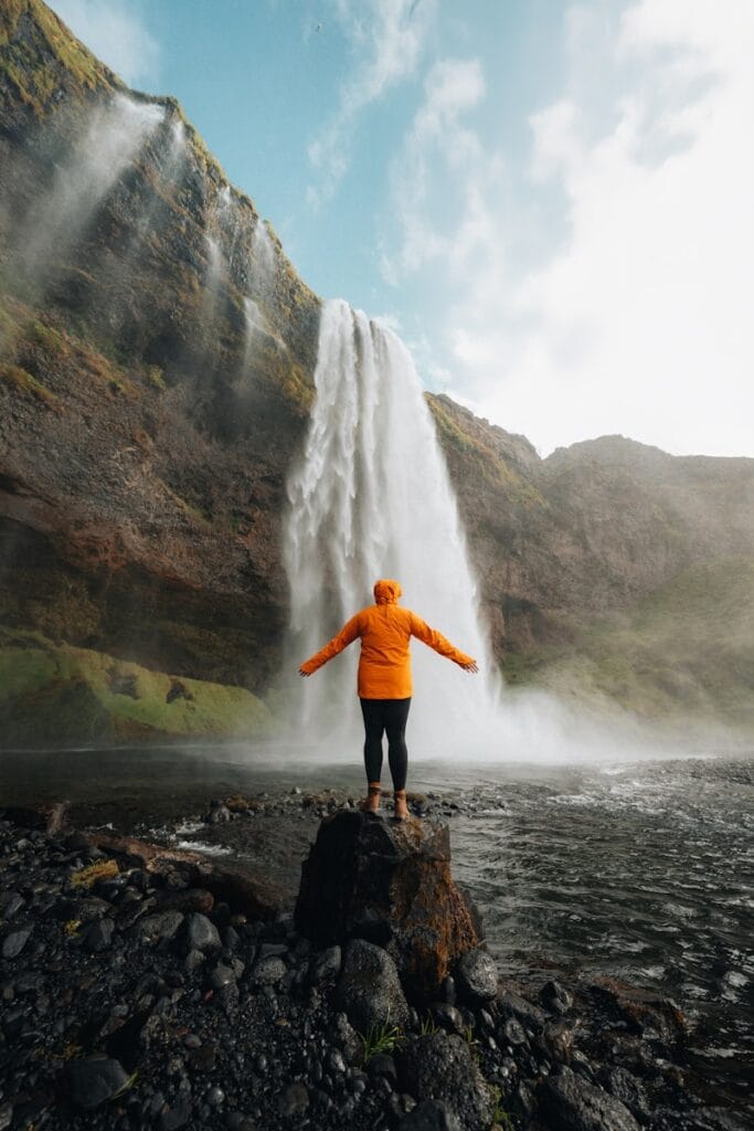 A person standing on a rock in front of a waterfall