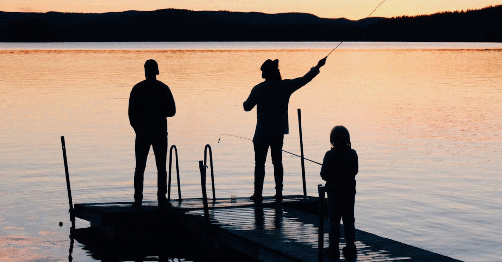 Family night fishing on a wooden dock at dusk.