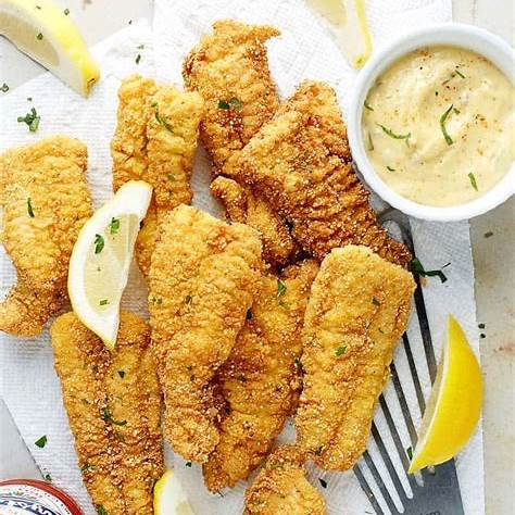 Plate of crispy fried catfish fillets served with lemon wedges and dipping sauce.
